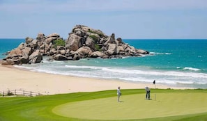 Campo de golf con una gran formación rocosa cerca de la playa y el océano.