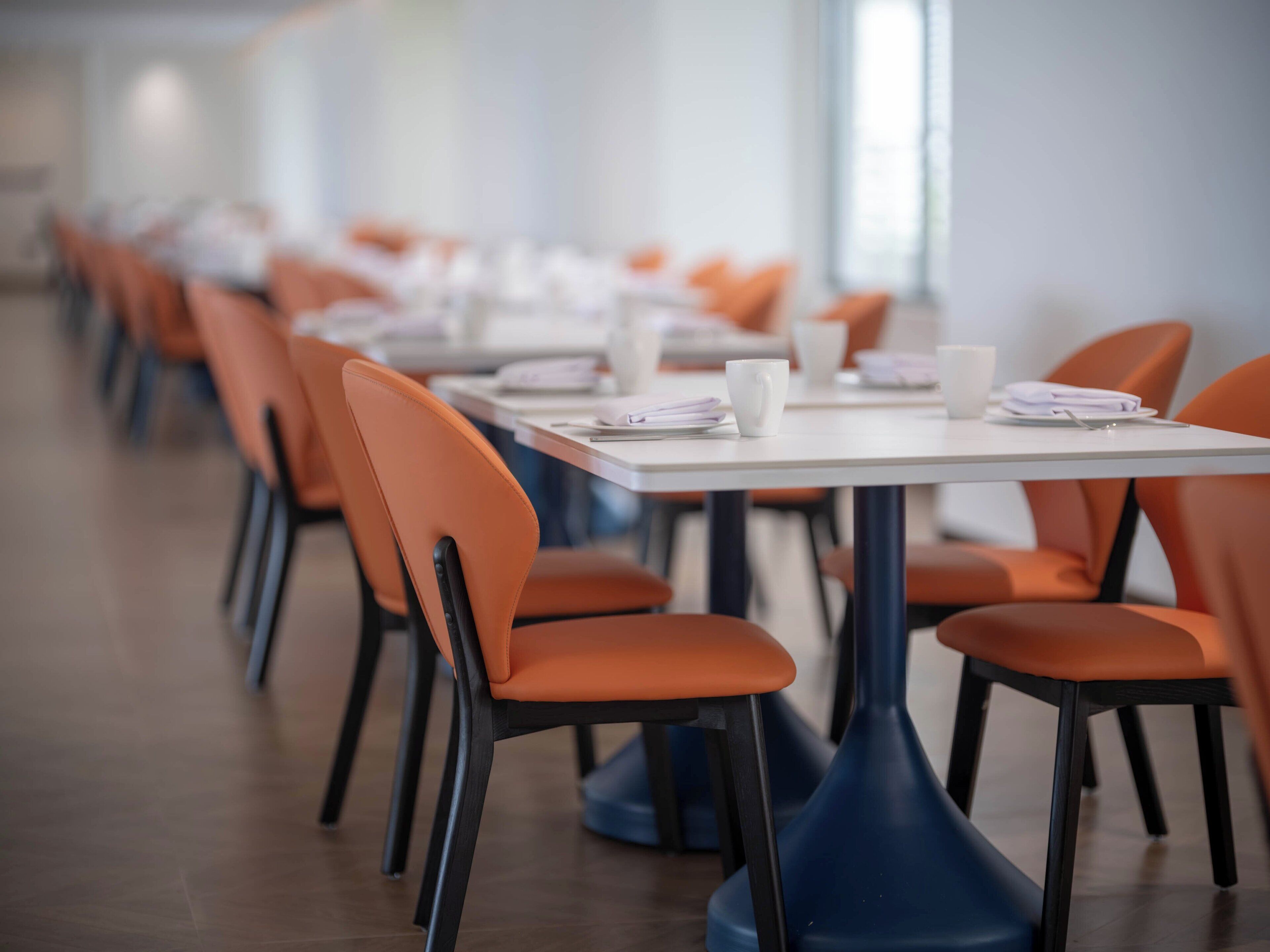 A row of tables with orange chairs in a modern, well-lit dining area.