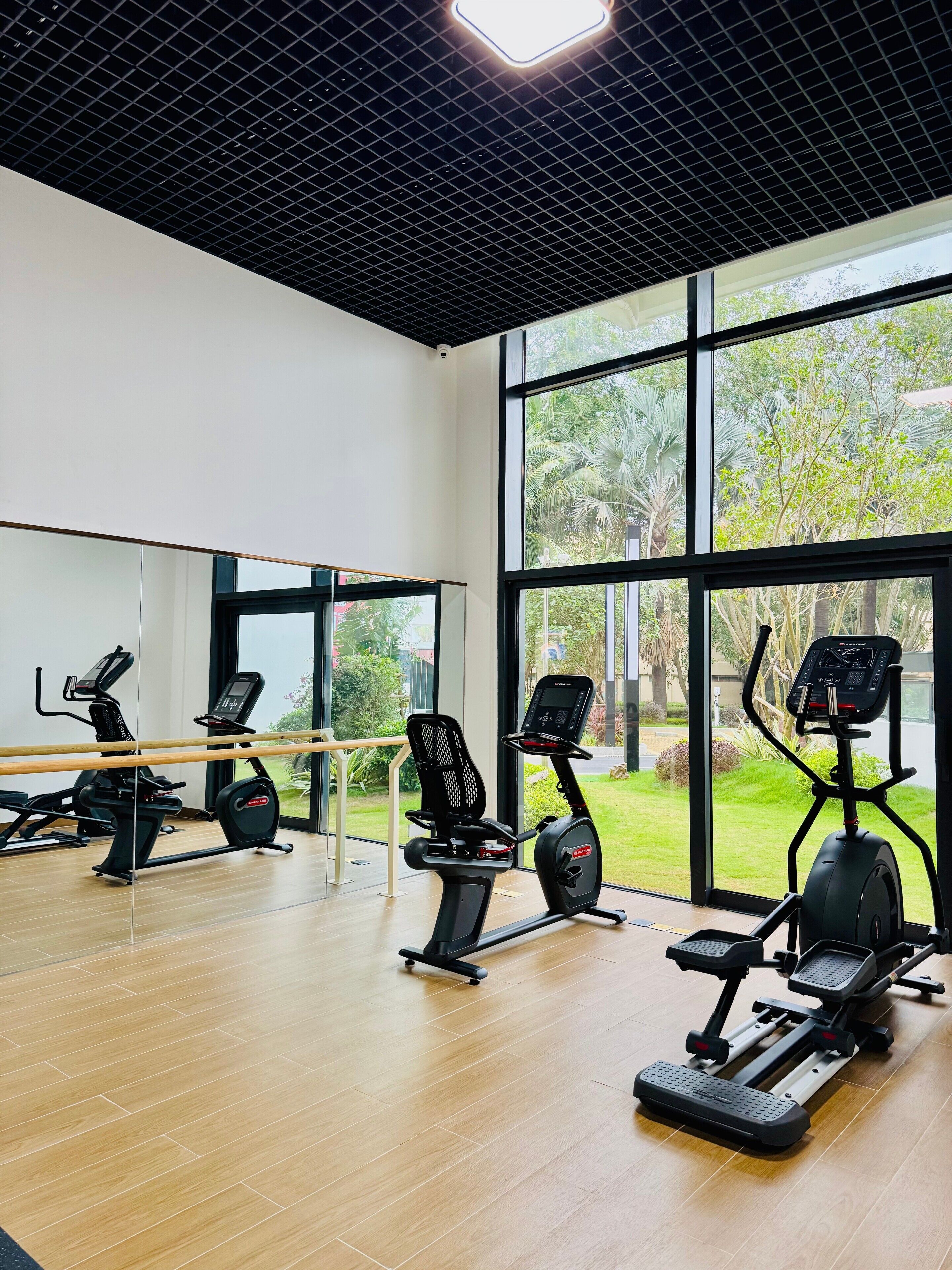 A gym with exercise equipment, large windows, and a wooden floor.