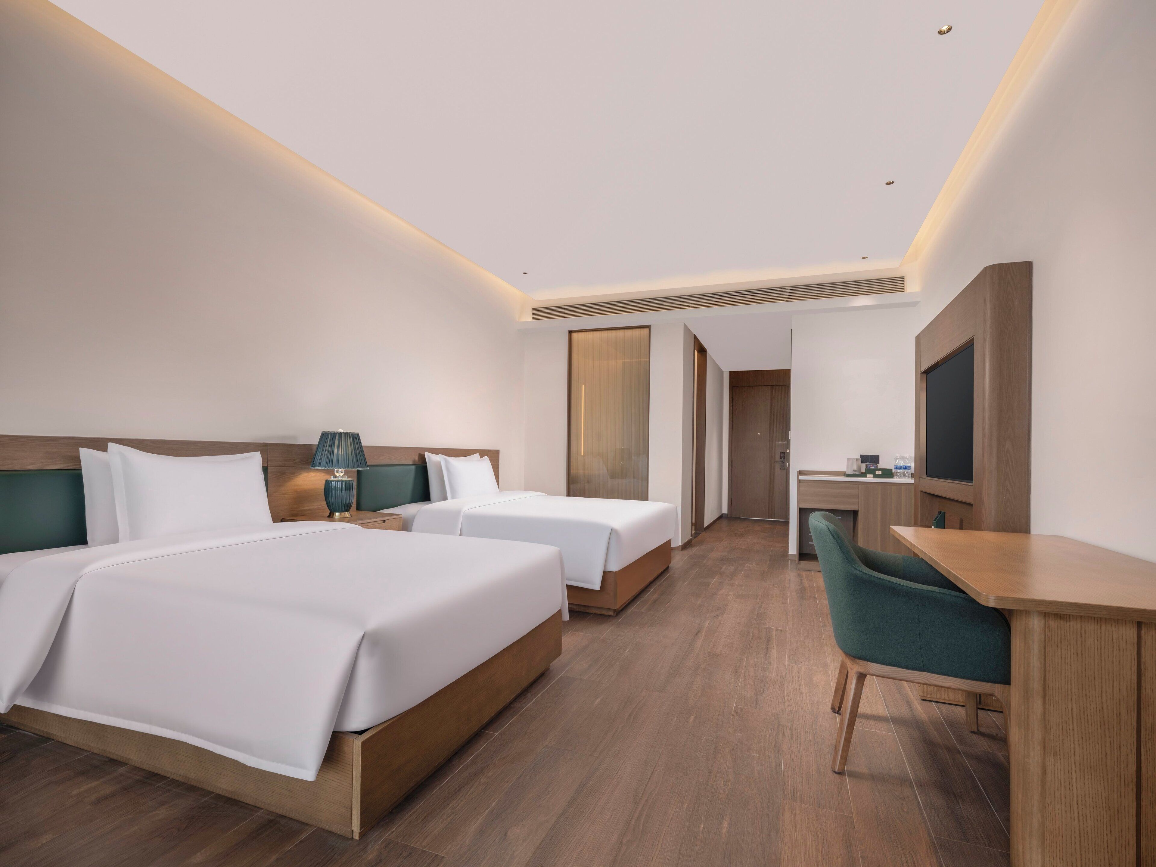 A modern hotel room with two beds, a desk, a chair, and a television.