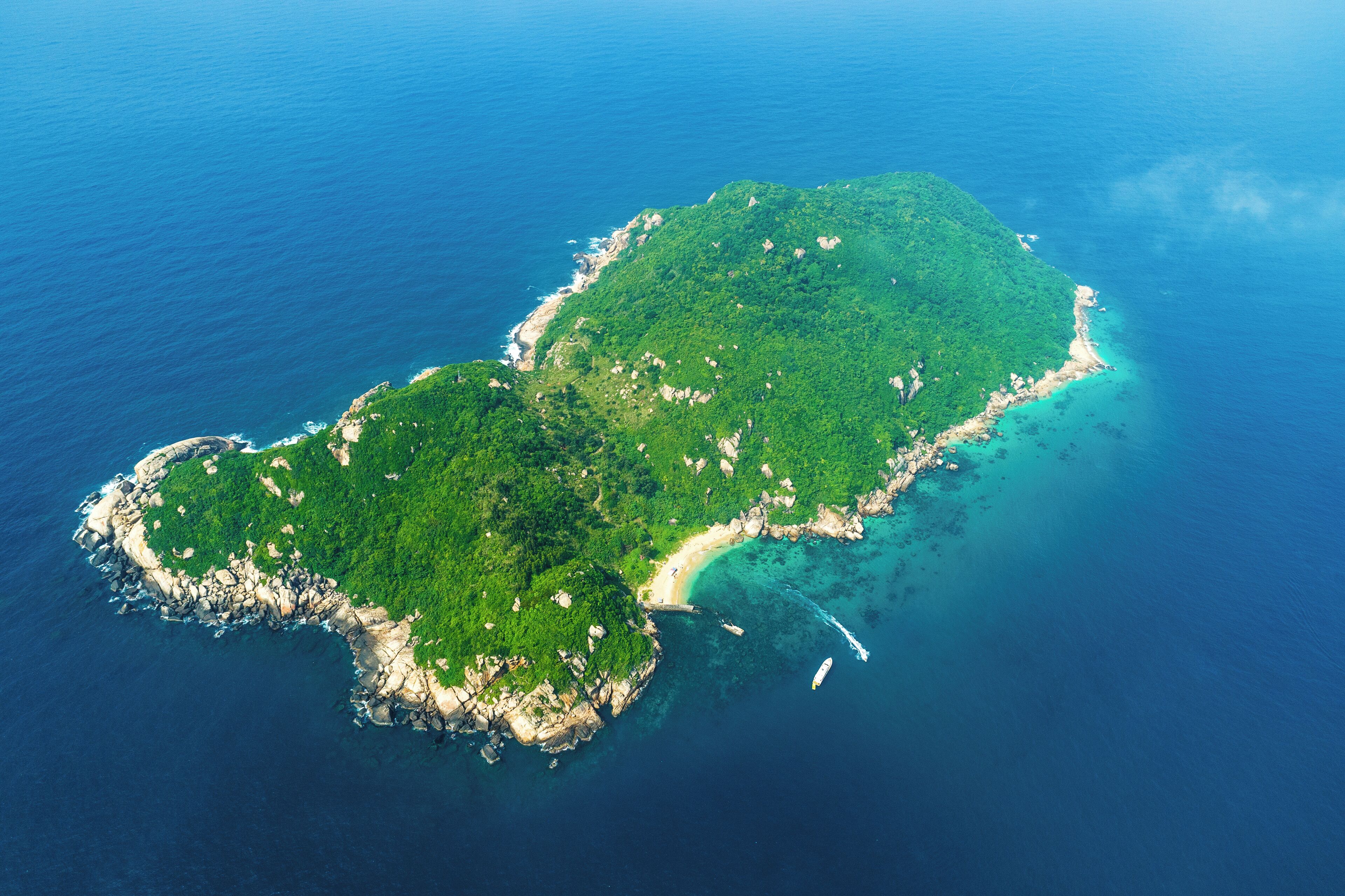 An aerial view of a tropical island with a beach, clear waters, and rocky coastline.