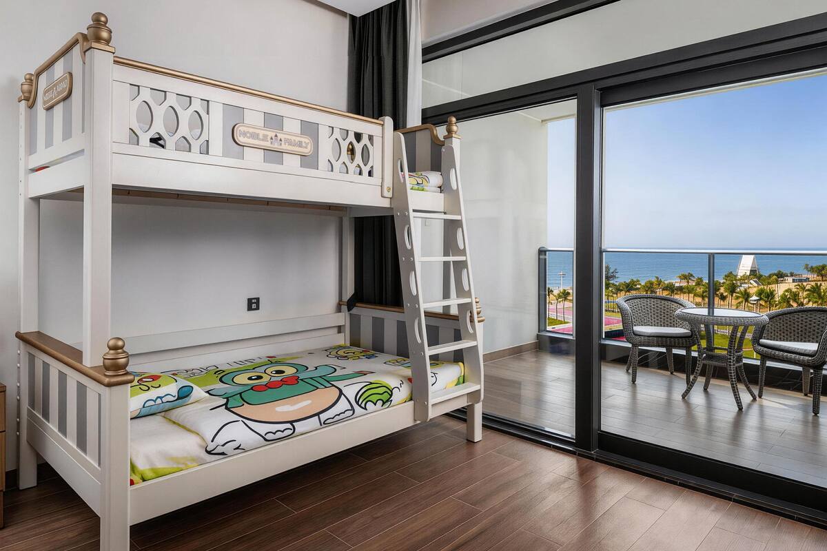 Una cama litera con escalera, una ventana que da a vista al océano y un balcón con sillas de mimbre.