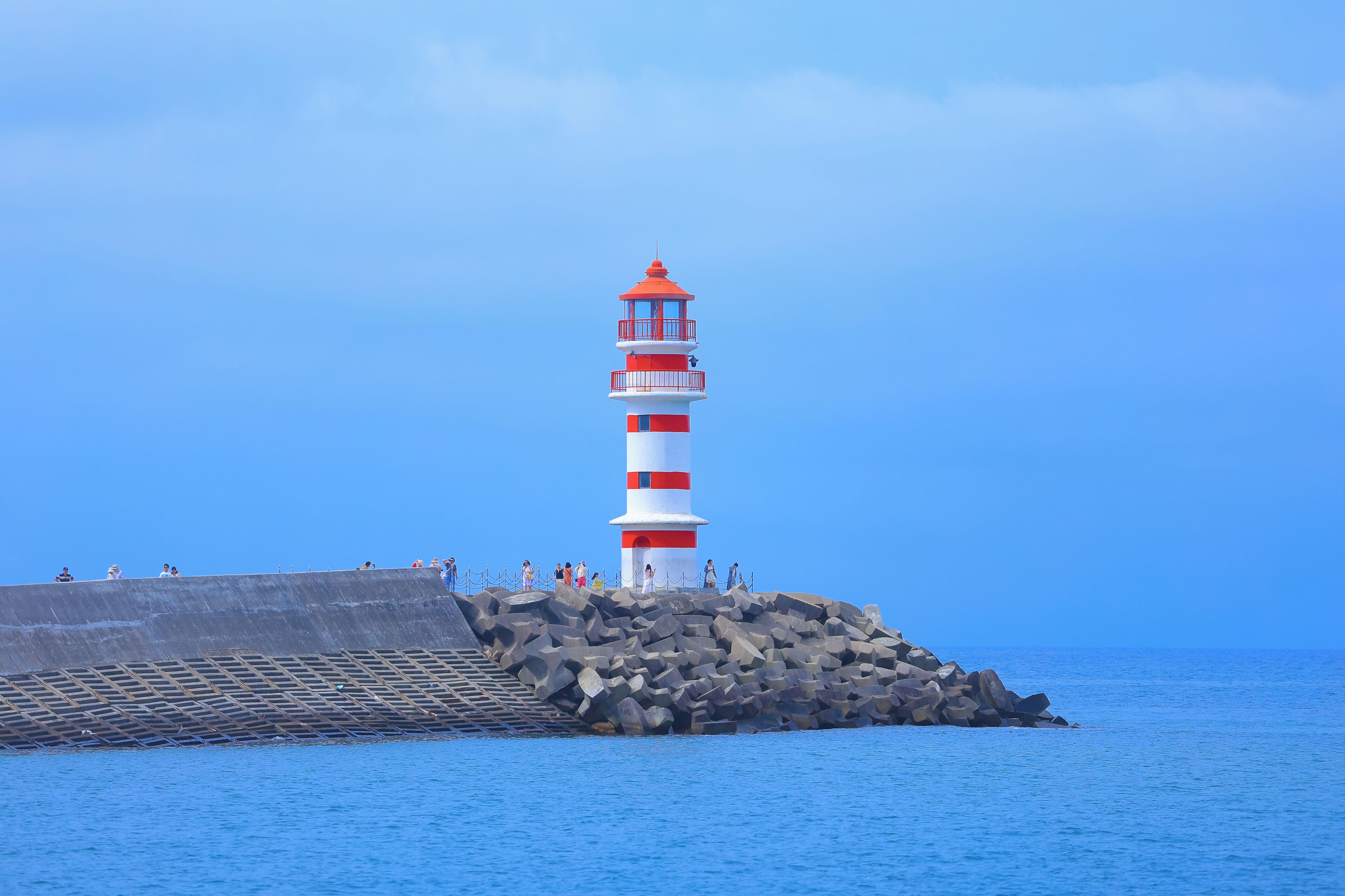 A lighthouse on a rocky outcrop with a clear blue sky.