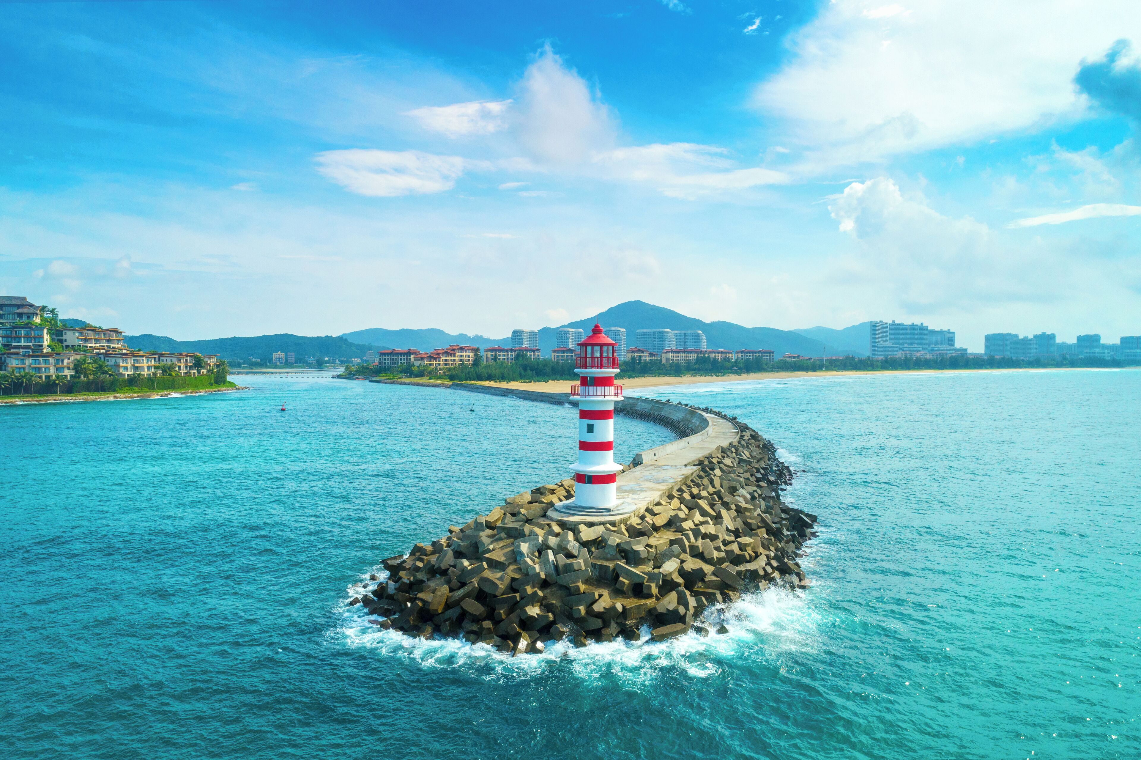 Un phare se dresse sur un promontoire rocheux au milieu d’une étendue d’eau, avec des bâtiments visibles à l’arrière-plan.