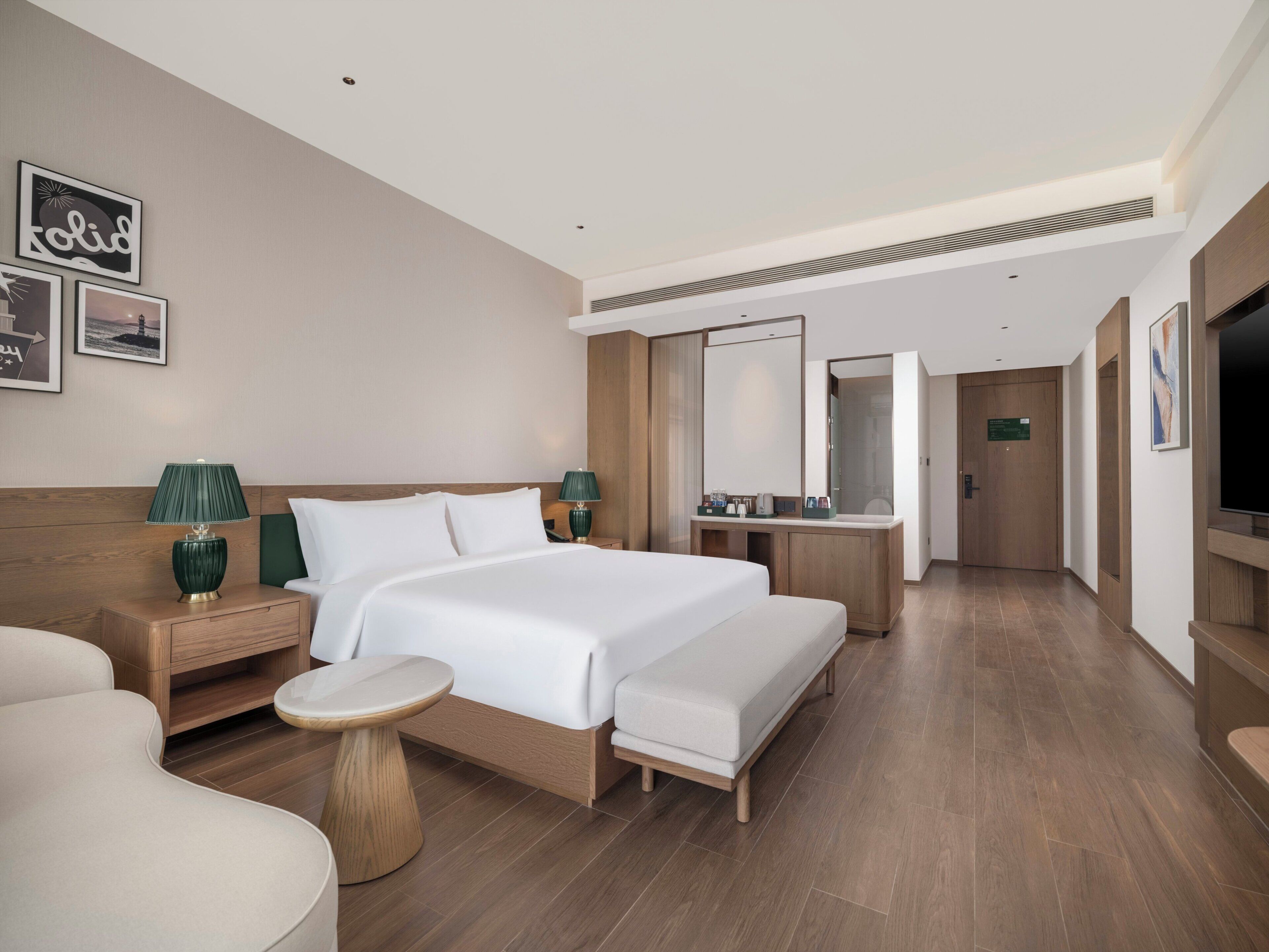 Una habitación de hotel moderna con una cama grande, una mesita de noche, una pequeña mesa redonda, un espejo y un televisor.