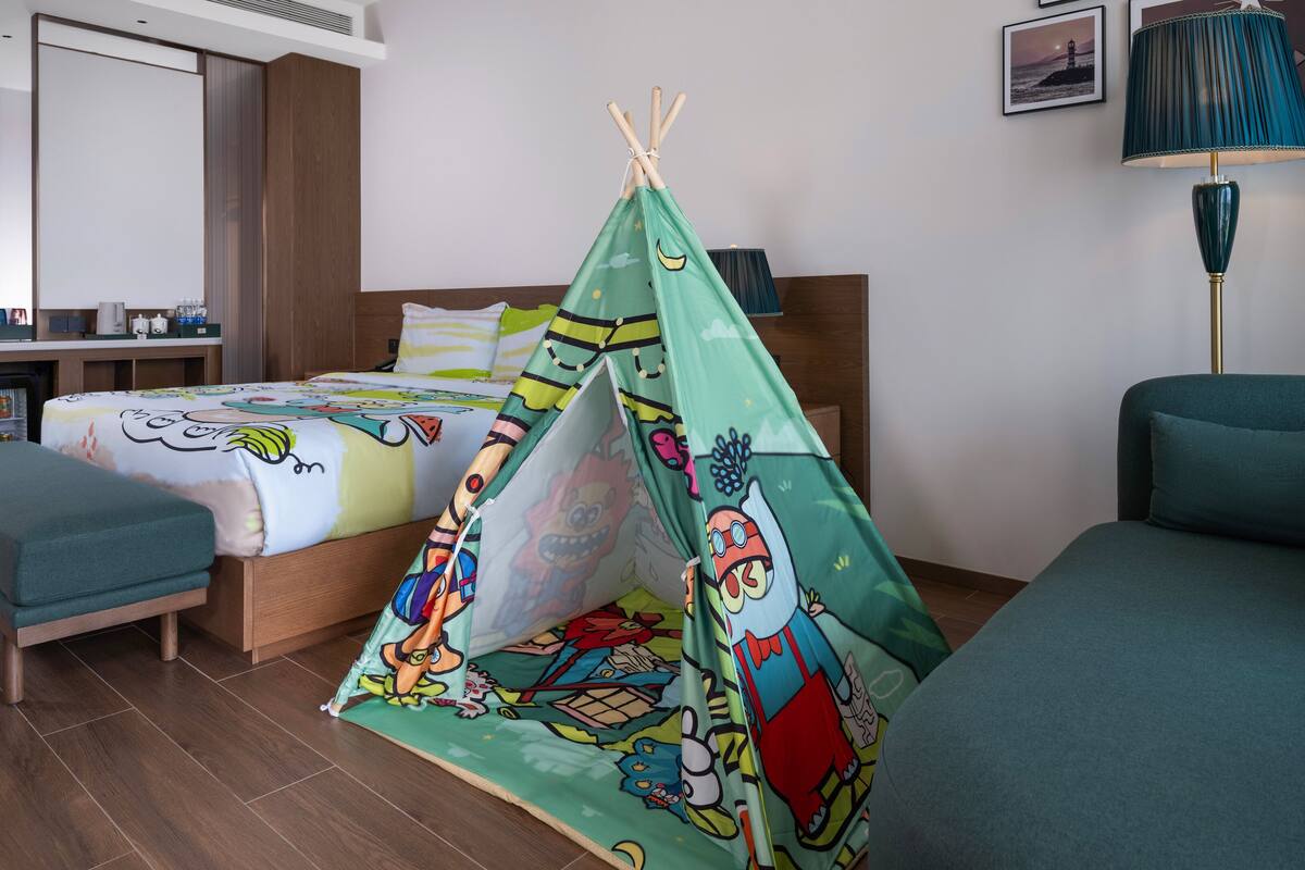 Una habitación con una cama, un escritorio pequeño, una silla, una estructura tipo tienda verde y una lámpara.