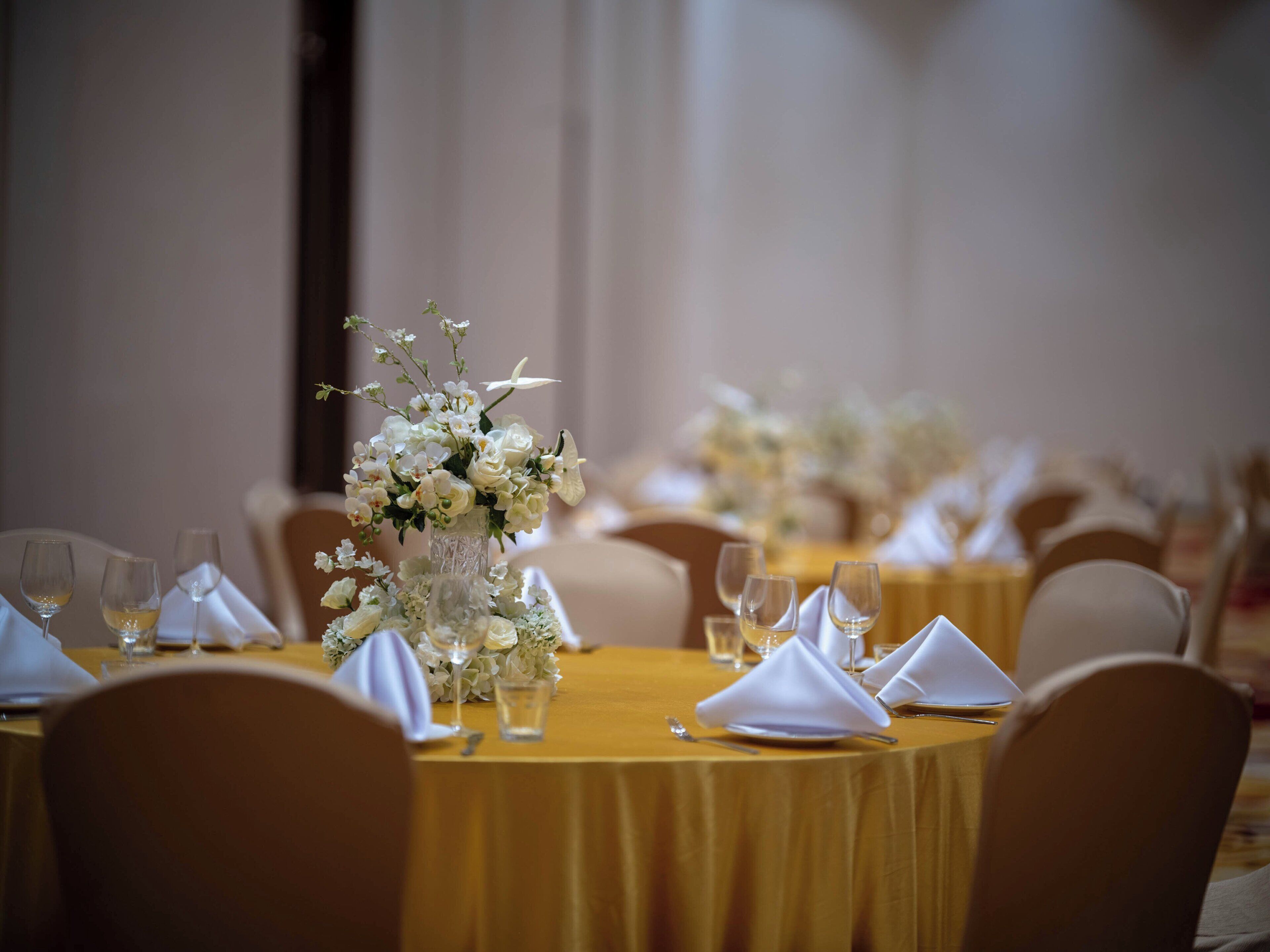 Una mesa de banquete dispuesta con flores blancas, copas de vino y servilletas dobladas.