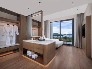 Ein modernes Hotelzimmer mit einem großen Bett, einem Schminktisch mit Spiegel, einem Badezimmer mit großem Fenster und Blick auf das Meer.