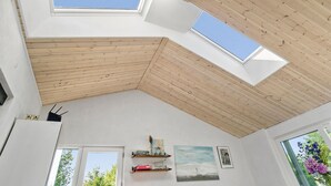 Una habitación con tragaluces, techo de madera, paredes blancas y obras de arte.