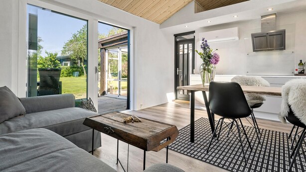 Una sala de estar moderna con un sofá gris, una mesa de centro de madera y un comedor con una silla negra y una butaca blanca de felpa.