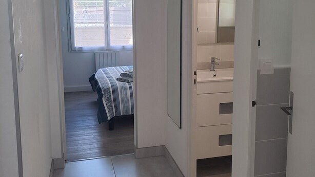 A hallway with a bed, a mirror, and a bathroom with a toilet and sink. - 1 minute from the beach! Apartment with terrace, ideal for families (La Tremblade)