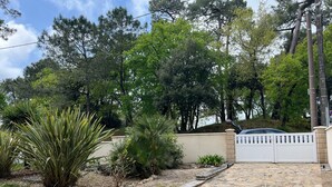 A stone pathway leading to a gated entrance, surrounded by various plants and trees. - 1 minute from the beach! Apartment with terrace, ideal for families (La Tremblade)