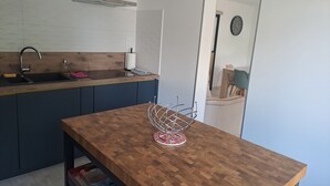 A modern kitchen with a wooden countertop, a sink, and a dining area with a table and chairs. - 1 minute from the beach! Apartment with terrace, ideal for families (La Tremblade)