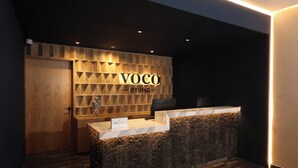 A reception desk with a wooden panel design and the name 'VOCO BY IHG' illuminated on the wall.