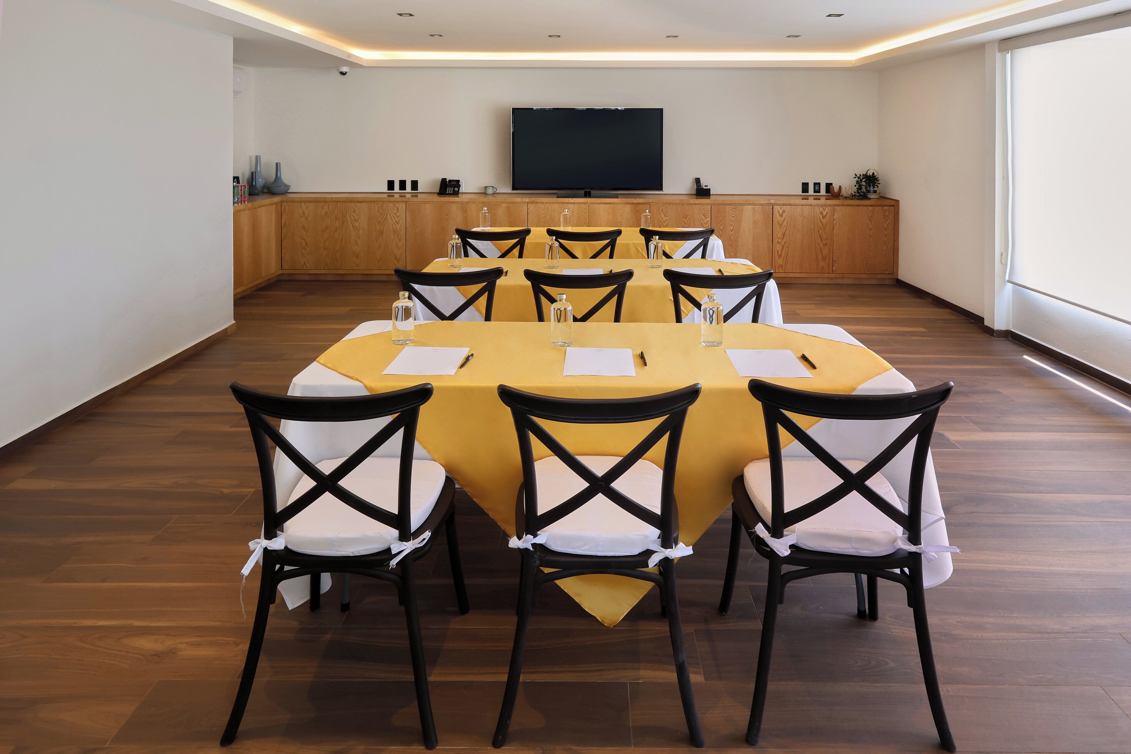 A conference room with a long table, chairs, a television, and a wooden cabinet.
