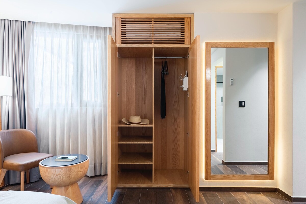 Una habitación de hotel con un armario de madera, una silla, una mesita redonda y una cama.