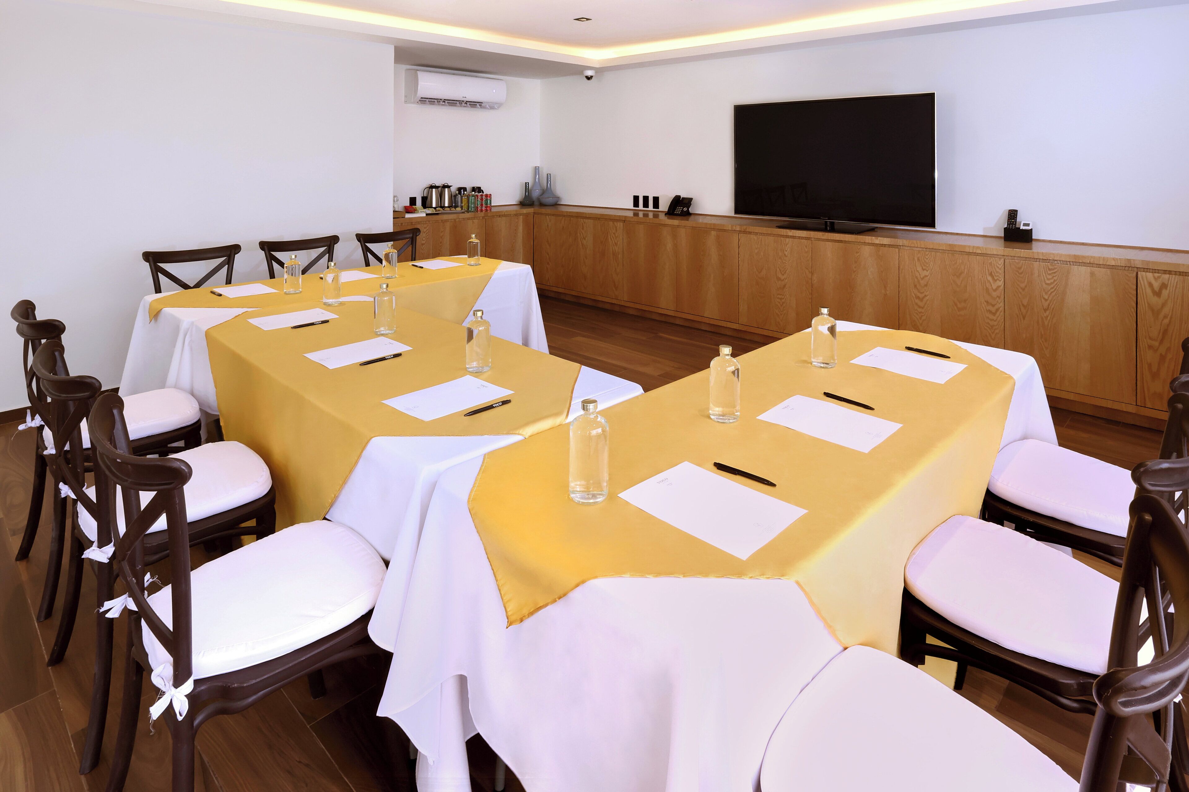 A conference room with multiple tables, chairs, a television, and a wooden paneling wall.