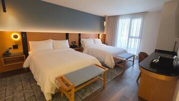 Ein Hotelzimmer mit zwei Betten, einem Schreibtisch, einem Sessel, einem kleinen Tisch und einem Fernseher.
