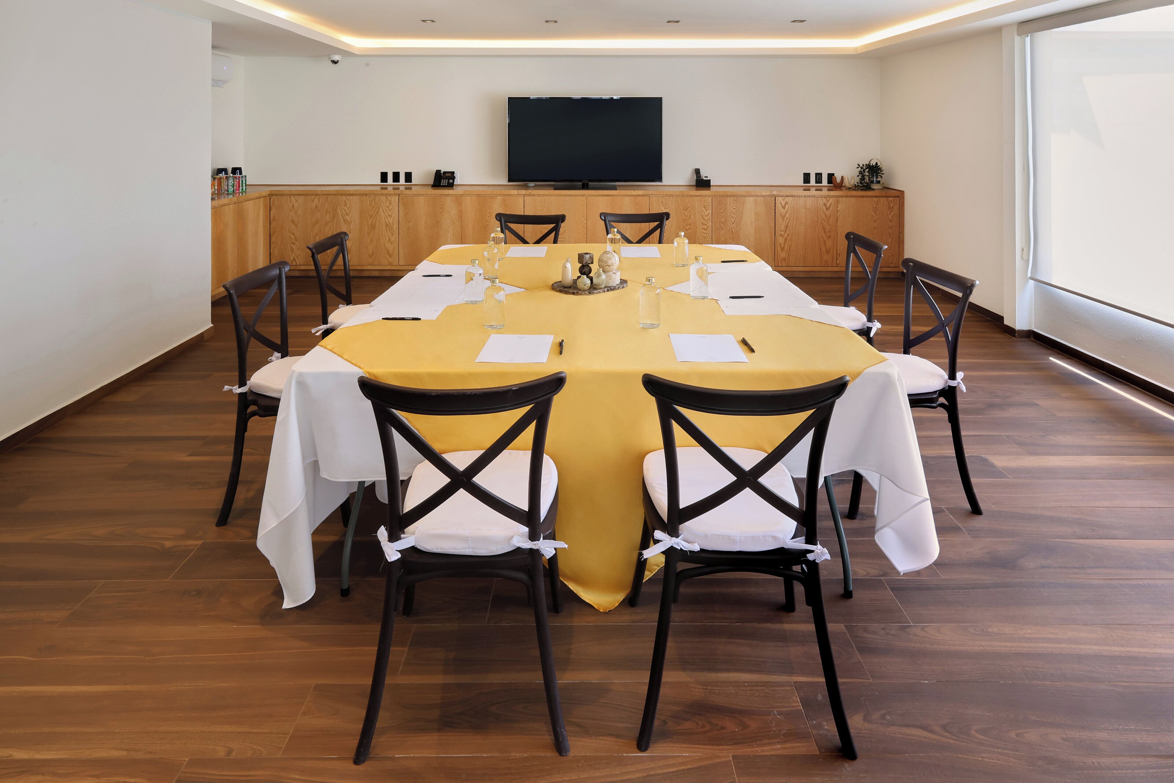 A conference room with a long table, chairs, a television, and a wooden cabinet.