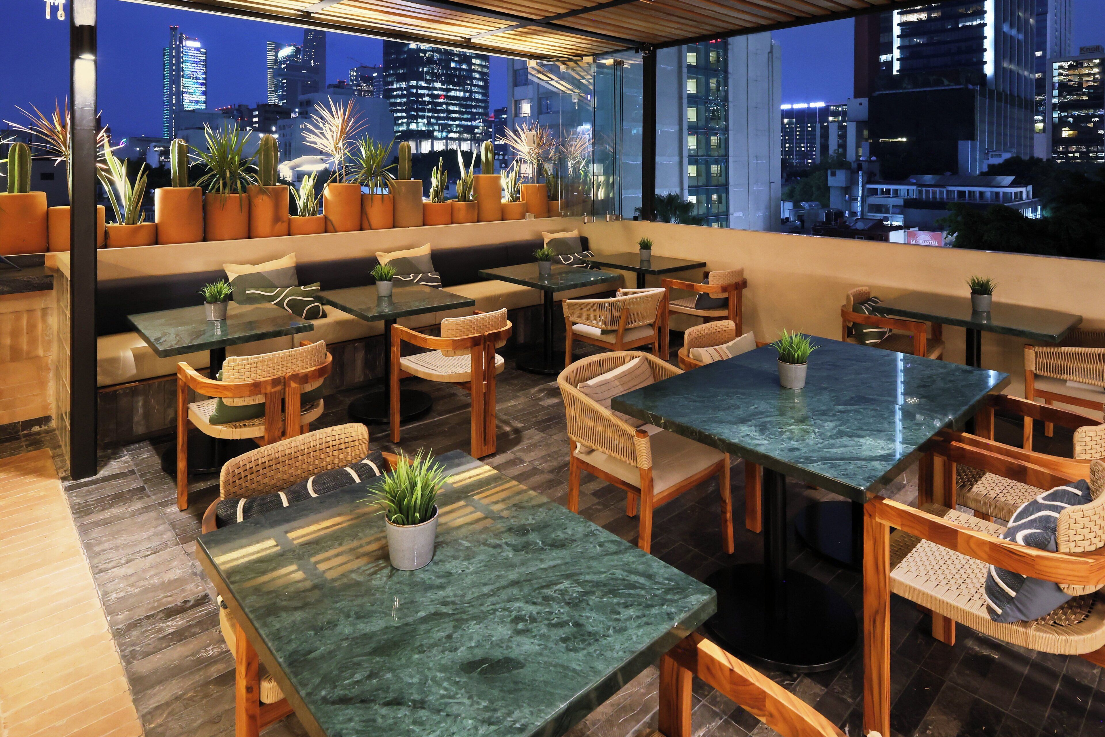 A rooftop bar with seating, tables, and potted plants.