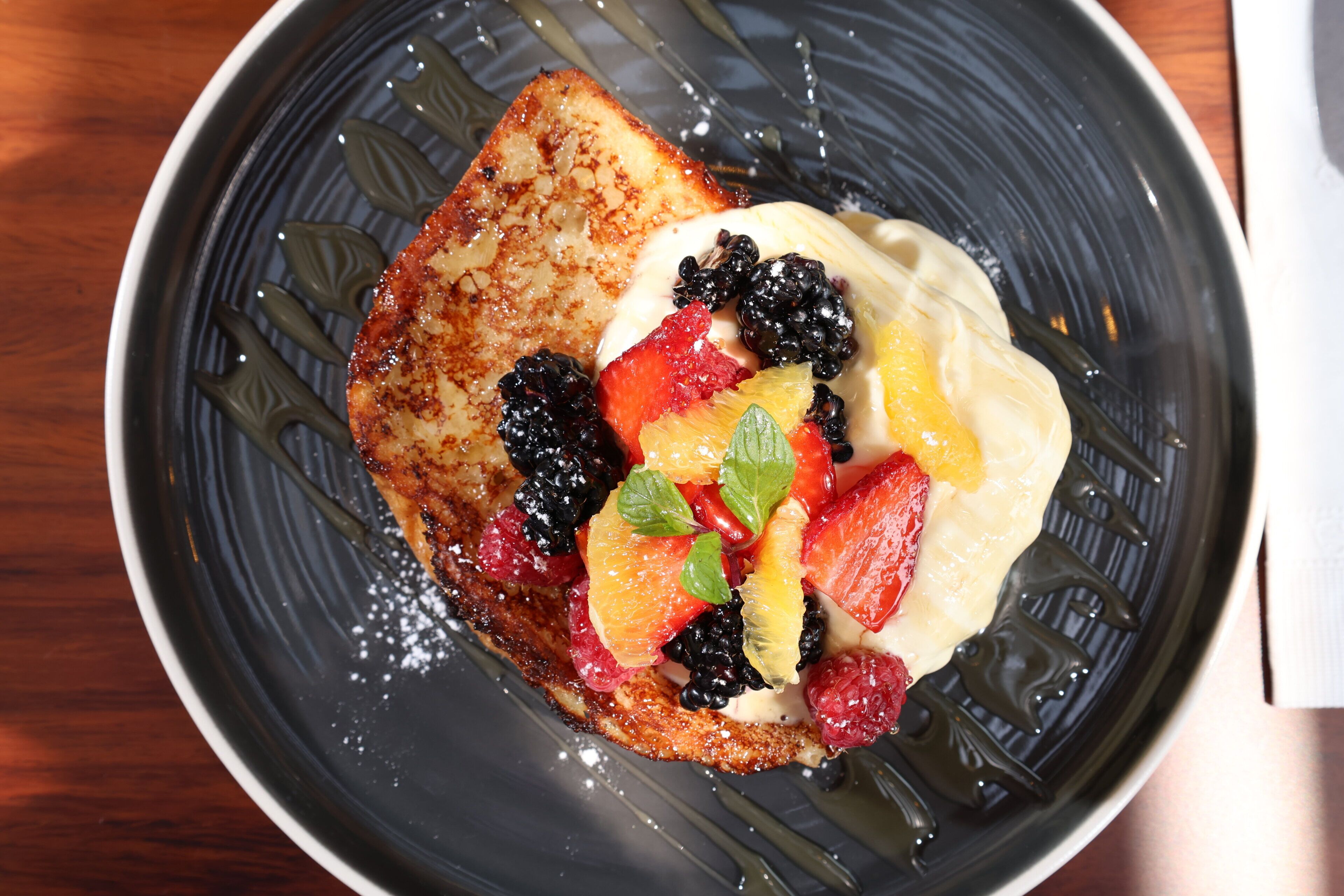 Une assiette avec des toasts, des fruits et de la crème fouettée.