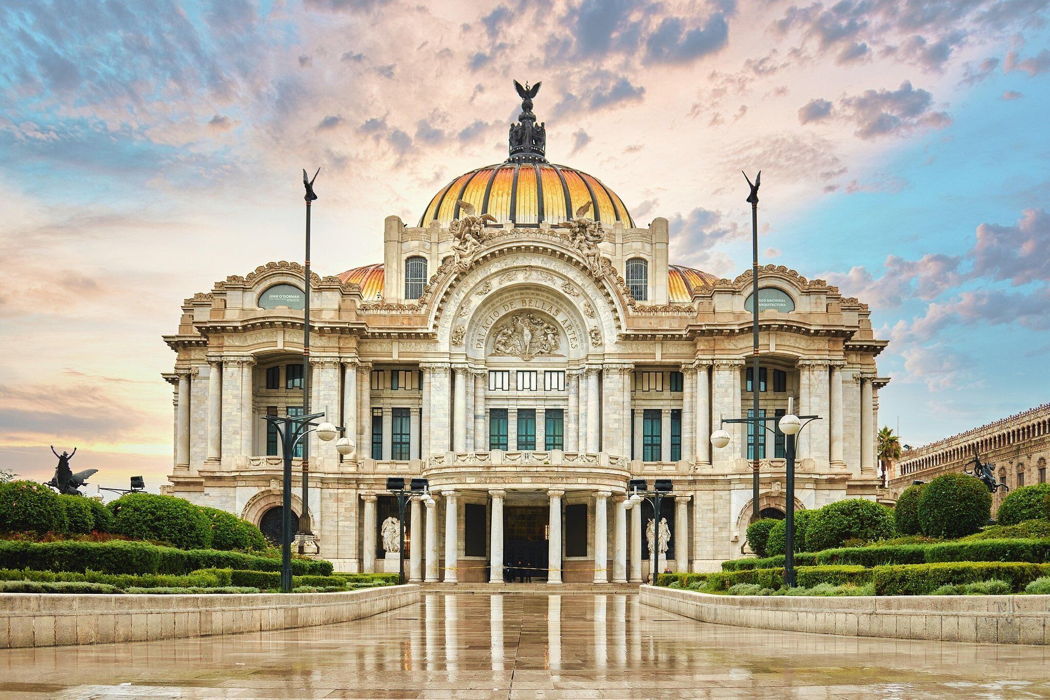 A grand building with a large dome and statues, featuring a central entrance with columns and a reflective courtyard.
