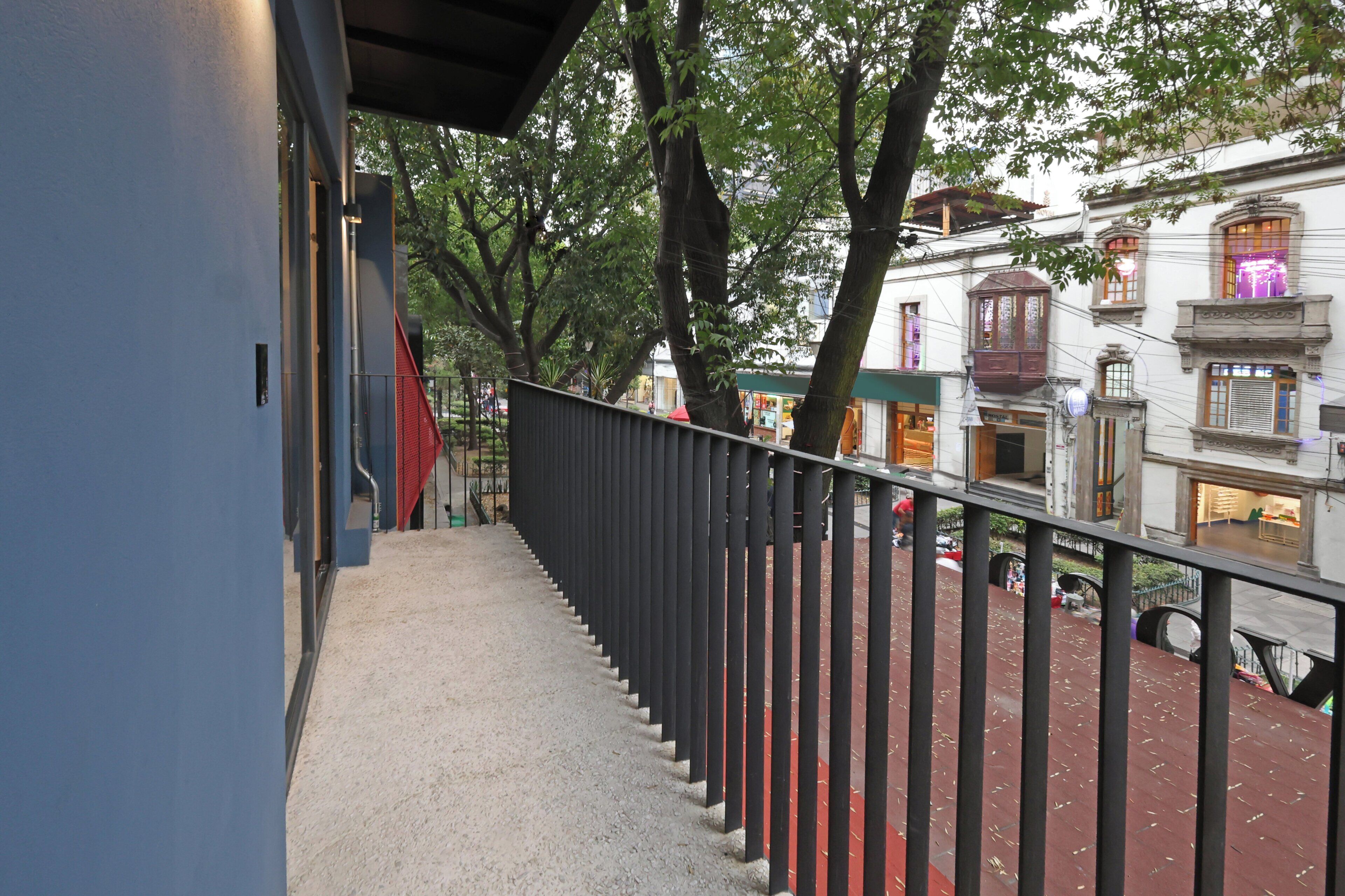 A balcony with a black railing overlooking a street with trees and buildings.