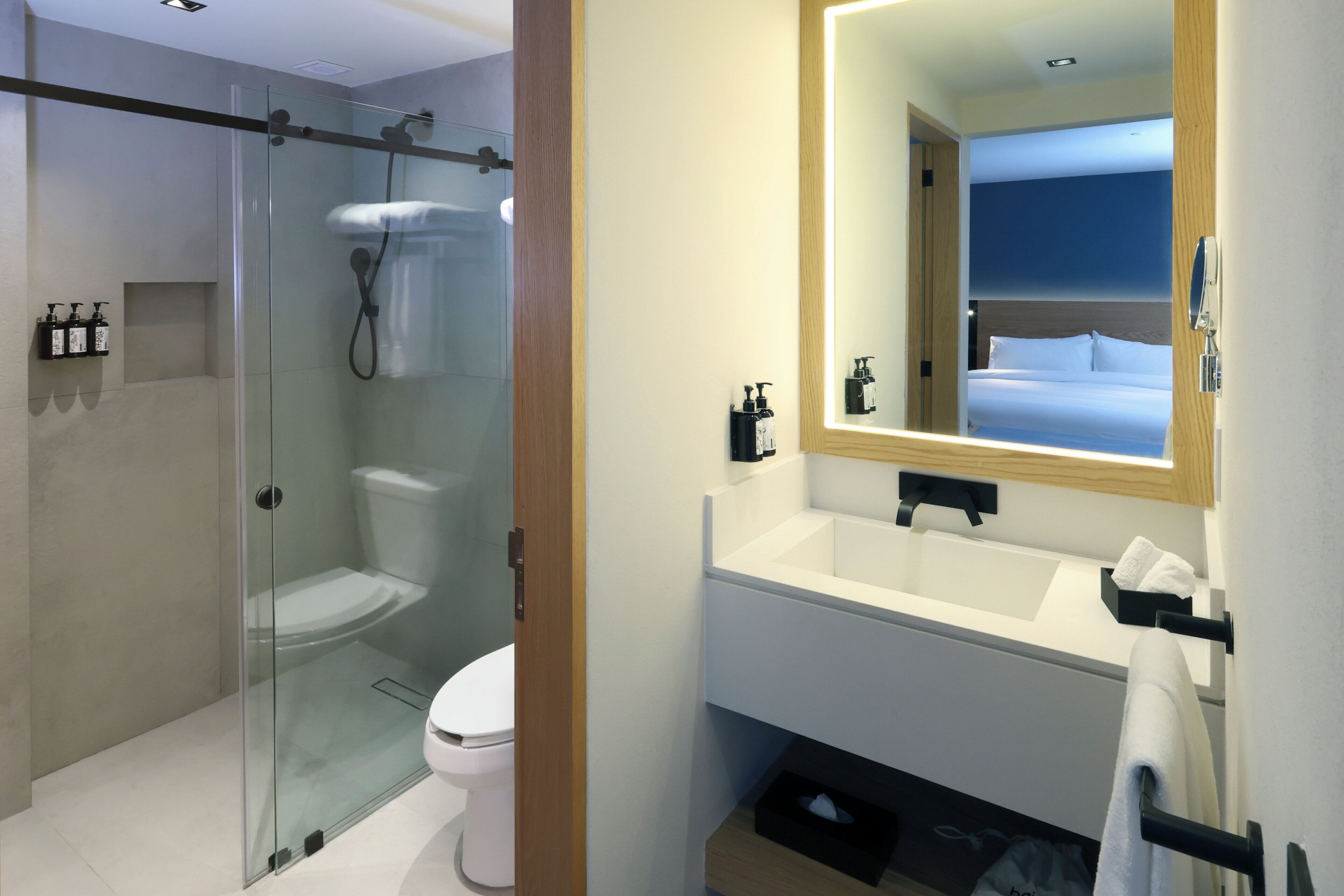A modern bathroom with a glass-enclosed shower, a white toilet, a large mirror, and a white sink.