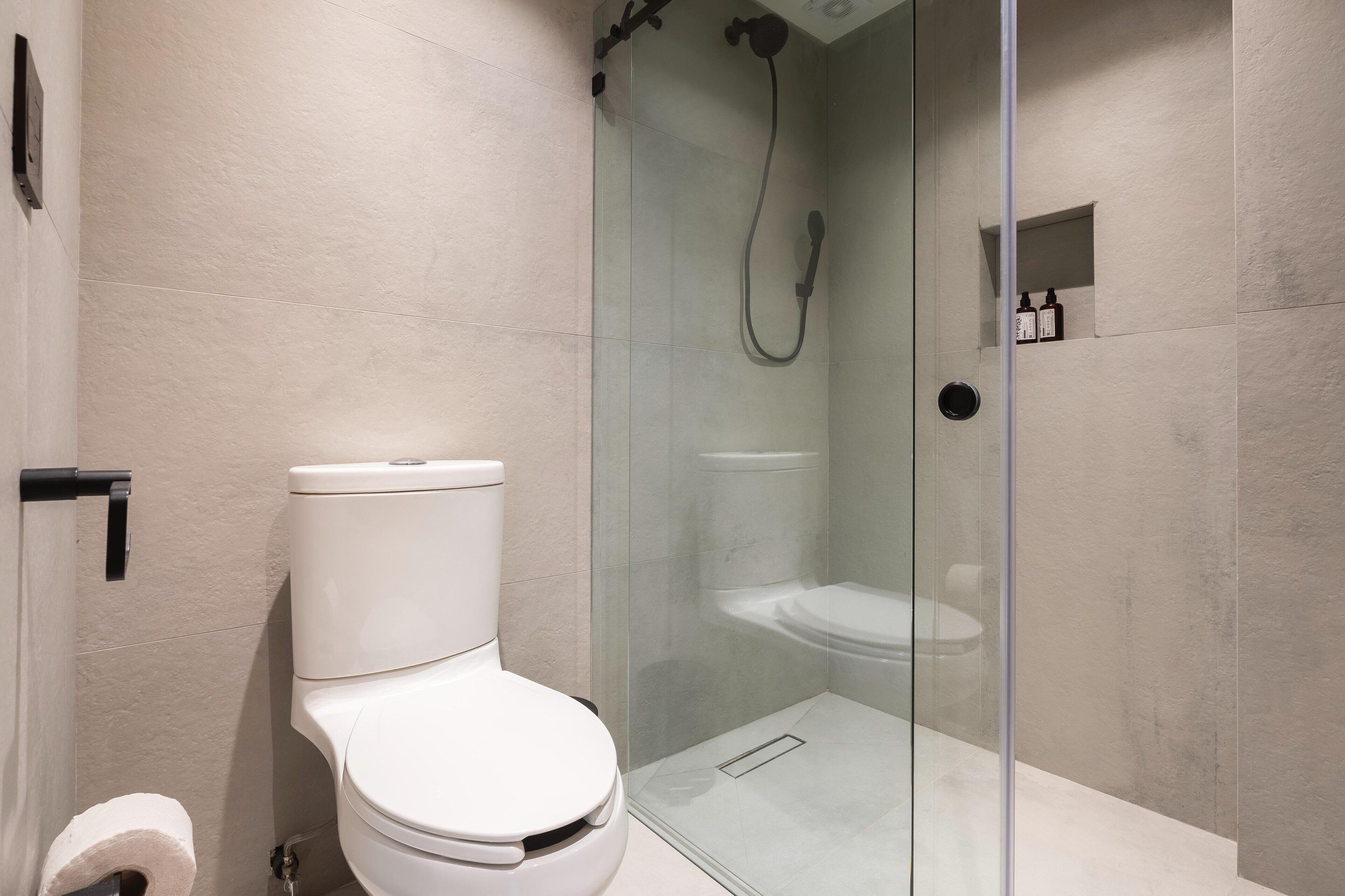 Une salle de bain moderne avec une douche à parois de verre, des toilettes et une petite étagère contenant des articles de toilette.