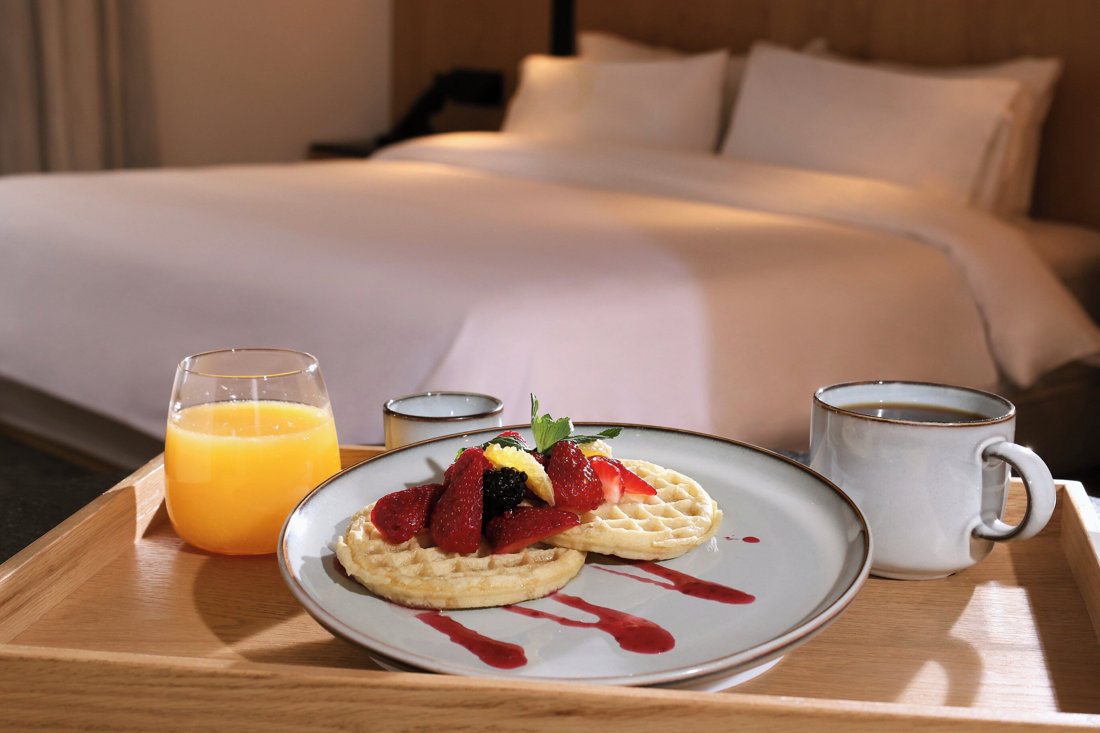 A breakfast tray with waffles, fruit, and juice on a wooden tray.