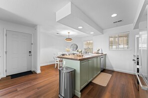 Una cocina moderna con una isla central, paredes blancas y suelo de madera.