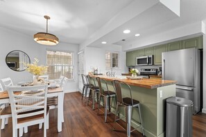 A modern kitchen with a central island, bar stools, a dining table with chairs, and a large mirror.