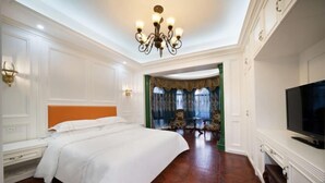 Een hotelkamer met een groot bed, een televisie, een kroonluchter en uitzicht op een eetgedeelte.