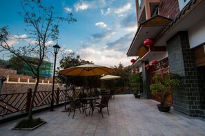 Un patio esterno con tavoli e sedie, vista sulla strada e un edificio con lanterne rosse.
