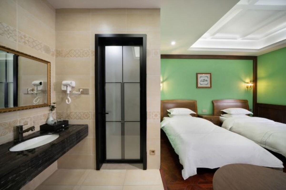Een hotelkamer met een badkamer, twee bedden, een spiegel en een groene wand.