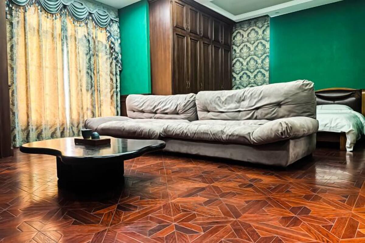 A room with a sofa, a coffee table, a bed, and patterned wallpaper.