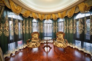 Ein Zimmer mit verzierten Vorhängen, zwei Stühlen und einem kleinen Tisch.