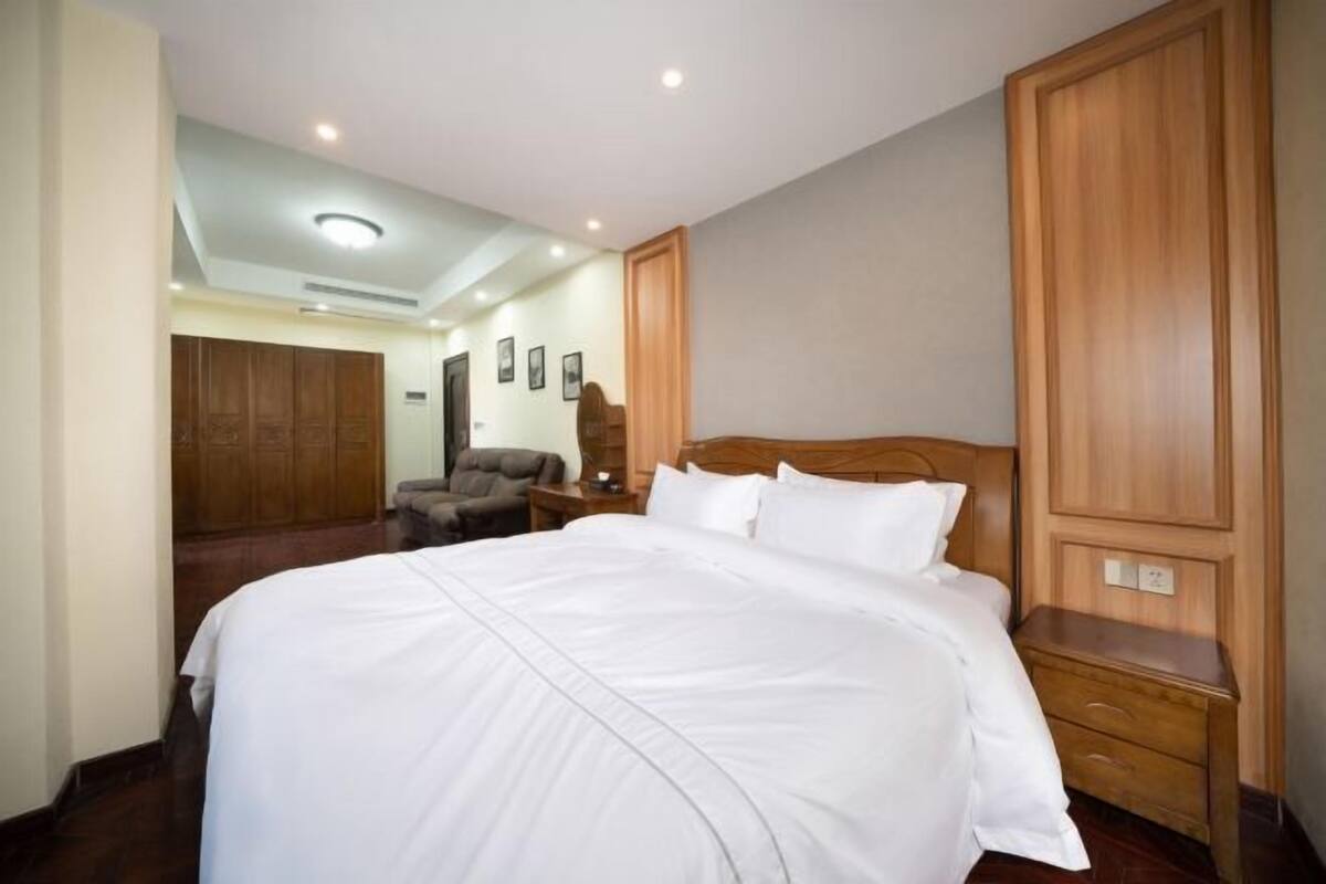 A hotel room with a large bed, wooden wardrobe, and a seating area with a chair and table.