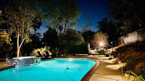 A swimming pool with a tiled edge, surrounded by trees and a covered area with seating. - Pacific Dreams at Woodland Hills Distinguished 8 Br 6 5 BA Residence With Pool and Spa Sleeps 16 (Calabasas)