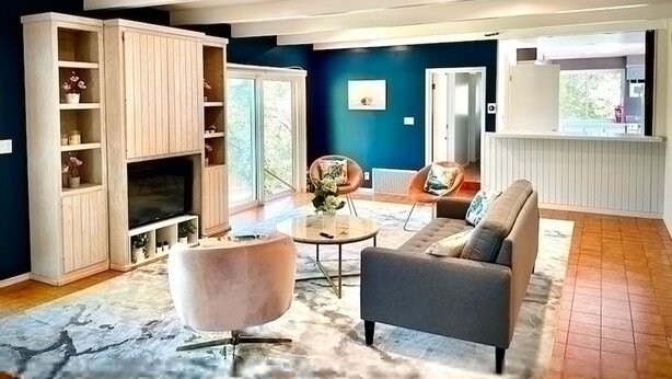 A modern living room with a sofa, a round coffee table, and a TV stand. There is a large window providing natural light and a view of the outdoors. - Pacific Dreams at Woodland Hills Distinguished 8 Br 6 5 BA Residence With Pool and Spa Sleeps 16 (Calabasas)