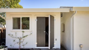 Una casa moderna con fachada blanca, puerta de madera y un pequeño jardín con una planta en maceta.
