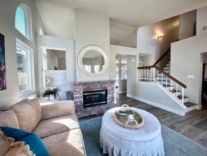 A spacious living room with a fireplace, a staircase, and a large mirror. - Crestview Oceanside - Family-friendly Private Yard (Oceanside)