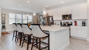 A modern kitchen with white cabinetry, a central island with bar stools, stainless steel appliances, and pendant lighting. - Ogl6008 (Davenport)
