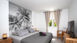 Une chambre à coucher avec un lit, une télévision, une table de chevet, une lampe et une fenêtre avec des rideaux.
