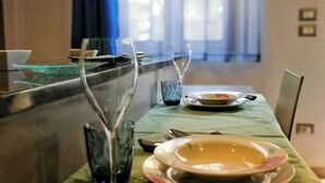A dining table set with plates, glasses, and cutlery, with a view of a window and curtains in the background. - The Sleeping Lions House (Pietrapiana)