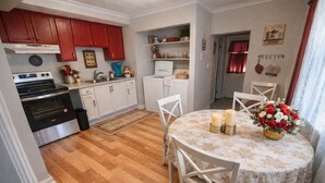 A kitchen with wooden flooring, white cabinets, a dining table with chairs, and a vase of flowers.
