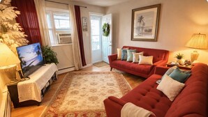 A living room with a red sofa, a TV on a stand, a patterned rug, and a door with a wreath.