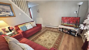 A living room with a red sofa, a patterned rug, a television, and a staircase in the background.