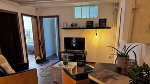 A living room with a TV, two chairs, a coffee table, and a bookshelf. - Private suite with sauna and garden (Etzling)