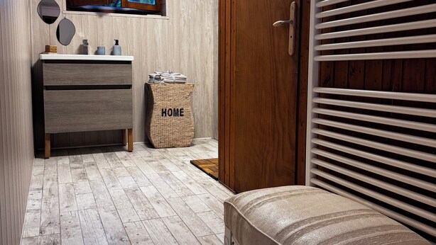 A bathroom with a wooden vanity, a bench, a window with a view, and a door with blinds. - Private suite with sauna and garden (Etzling)